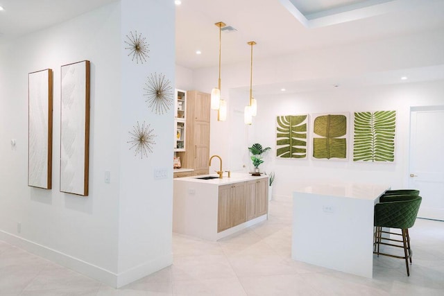 kitchen with light brown cabinetry, a kitchen breakfast bar, pendant lighting, sink, and a kitchen island with sink