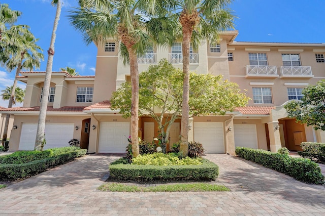 townhome / multi-family property with a tiled roof, decorative driveway, an attached garage, and stucco siding