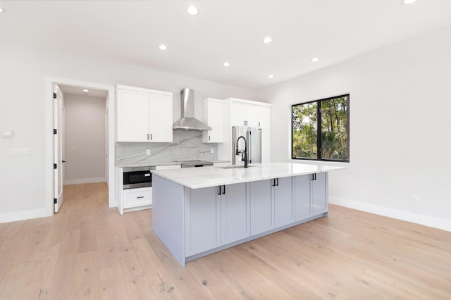 kitchen with white cabinetry, a large island, light stone countertops, appliances with stainless steel finishes, and wall chimney exhaust hood