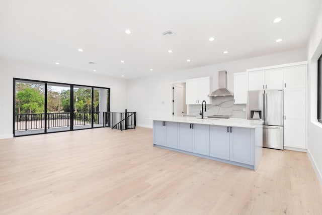 kitchen featuring a large island, stainless steel fridge with ice dispenser, wall chimney exhaust hood, white cabinets, and decorative backsplash