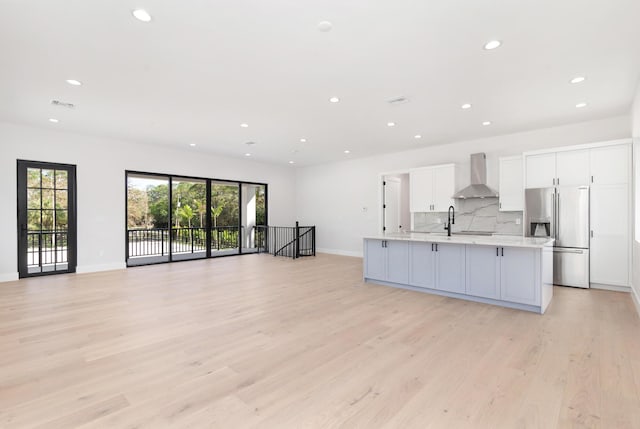 kitchen featuring white cabinetry, a large island, stainless steel fridge with ice dispenser, wall chimney range hood, and decorative backsplash