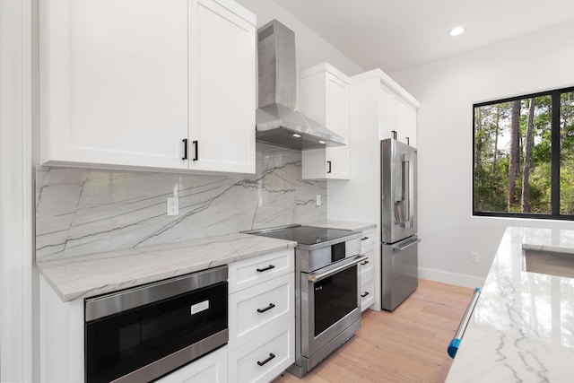 kitchen featuring white cabinetry, wall chimney range hood, stainless steel appliances, and light stone counters