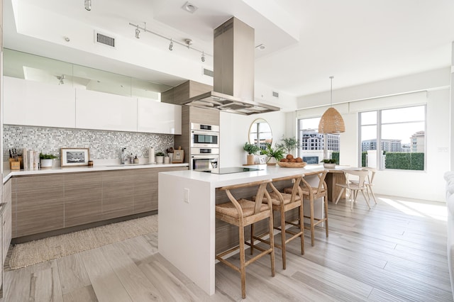 kitchen with white cabinetry, a breakfast bar, a kitchen island, backsplash, and island range hood