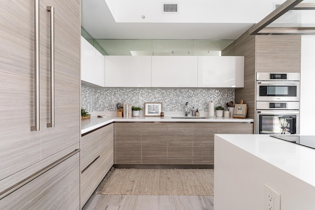 kitchen with double oven, decorative backsplash, sink, and white cabinets