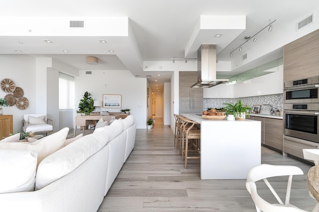 kitchen with a kitchen bar, light hardwood / wood-style flooring, backsplash, island range hood, and stainless steel double oven