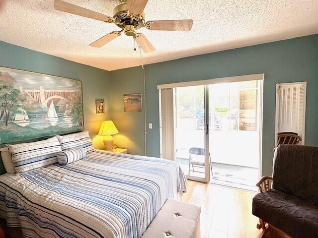 bedroom with a textured ceiling, access to outside, wood finished floors, and a ceiling fan