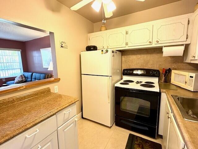 kitchen with light tile patterned floors, a ceiling fan, white cabinetry, a sink, and white appliances