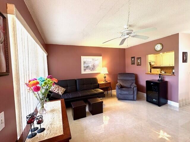 living room with vaulted ceiling, a textured ceiling, baseboards, and ceiling fan