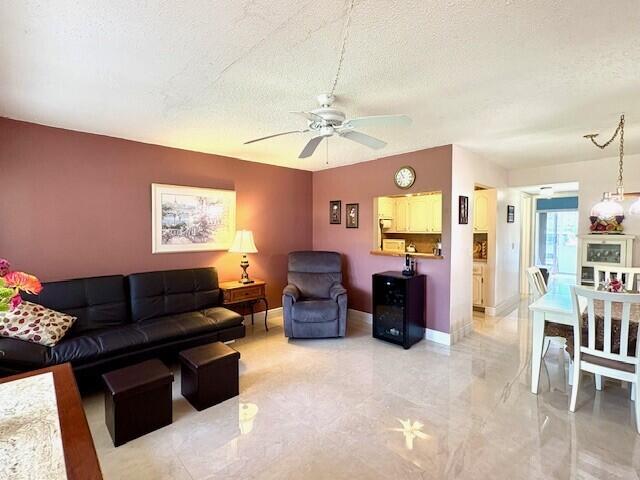 living room with a ceiling fan, baseboards, and a textured ceiling