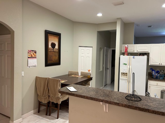 1732 SW Alegre St, Port Saint Lucie, FL 34953 - kitchen with white refrigerator with ice dispenser, visible vents, dark countertops, arched walkways, and white cabinets