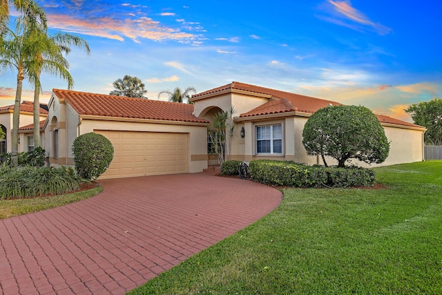 mediterranean / spanish-style home featuring a garage, a tile roof, decorative driveway, a yard, and stucco siding