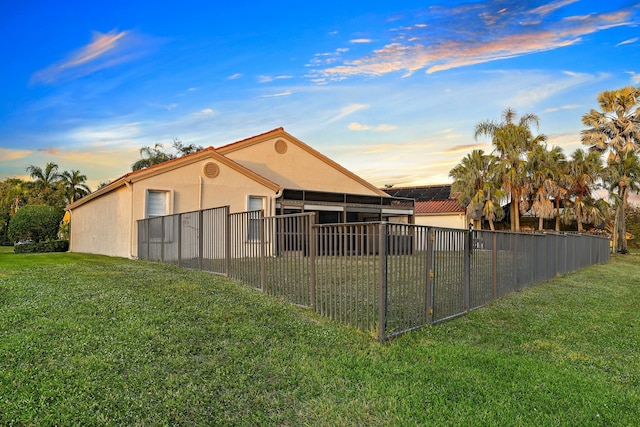 back of house at dusk with a yard, fence, and stucco siding