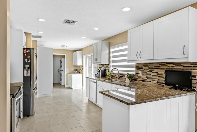 kitchen with stainless steel appliances, a peninsula, a sink, visible vents, and dark stone countertops