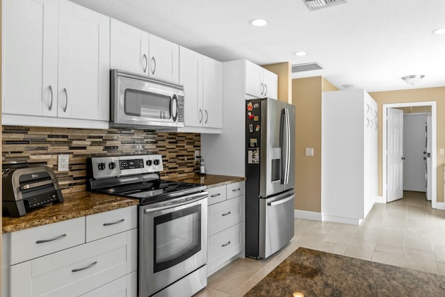 kitchen with tasteful backsplash, stainless steel appliances, dark stone countertops, and light tile patterned flooring