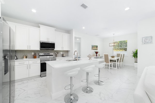 kitchen with appliances with stainless steel finishes, decorative light fixtures, a breakfast bar, and white cabinets