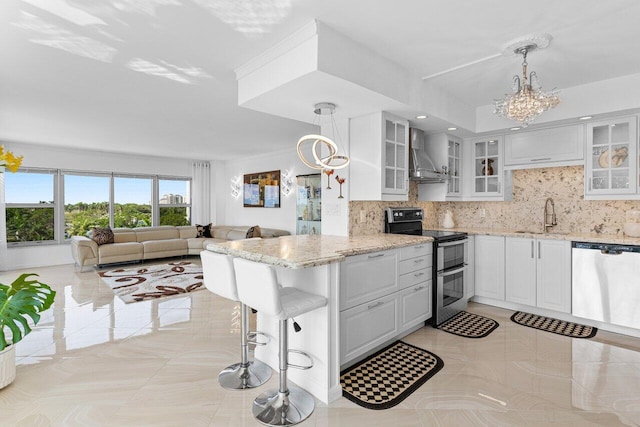 875 E Camino Real Unit 7E, Boca Raton, FL 33432 - kitchen featuring white cabinetry, appliances with stainless steel finishes, wall chimney range hood, and pendant lighting