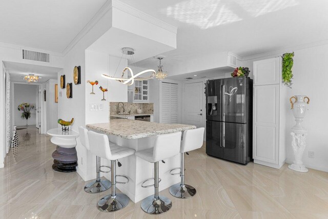 875 E Camino Real Unit 7E, Boca Raton, FL 33432 - kitchen with white cabinets, decorative light fixtures, a breakfast bar, black fridge, and kitchen peninsula