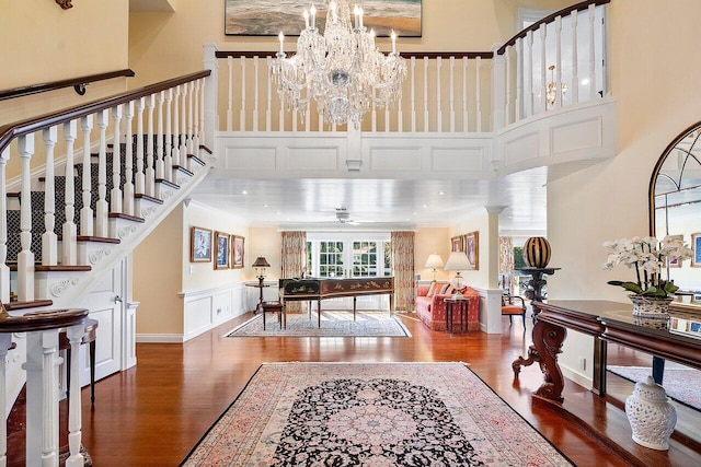 entrance foyer featuring crown molding, dark wood finished floors, ceiling fan with notable chandelier, stairs, and a high ceiling