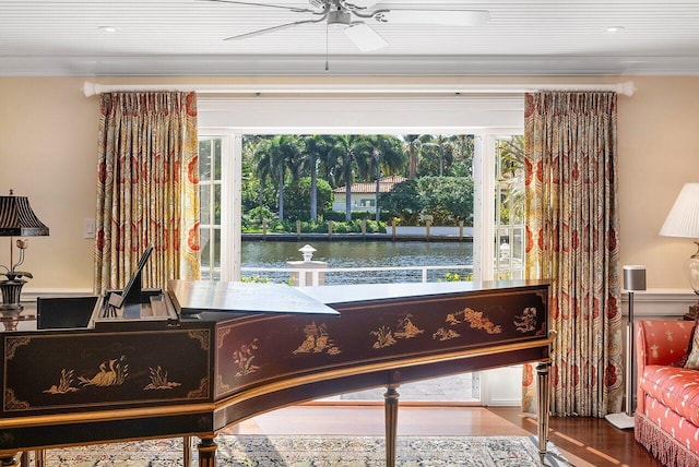 living area with plenty of natural light, wood finished floors, a water view, and ornamental molding