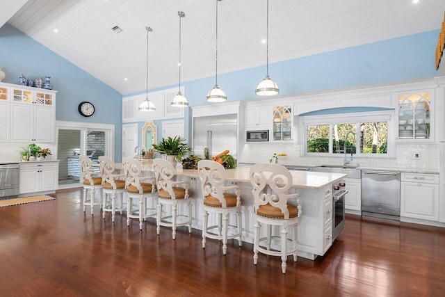 kitchen featuring hanging light fixtures, a kitchen island, glass insert cabinets, white cabinetry, and appliances with stainless steel finishes