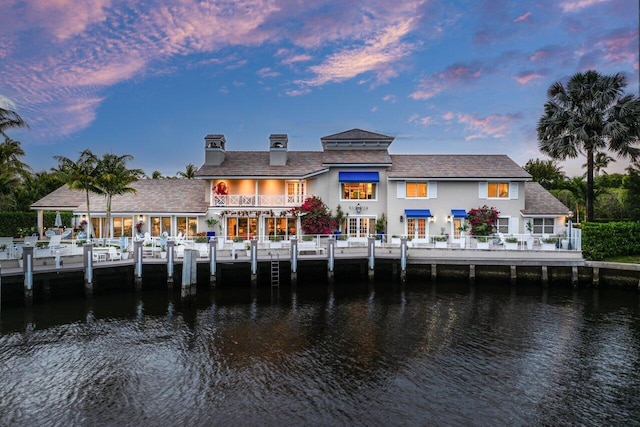 back of house at dusk featuring a balcony and a water view