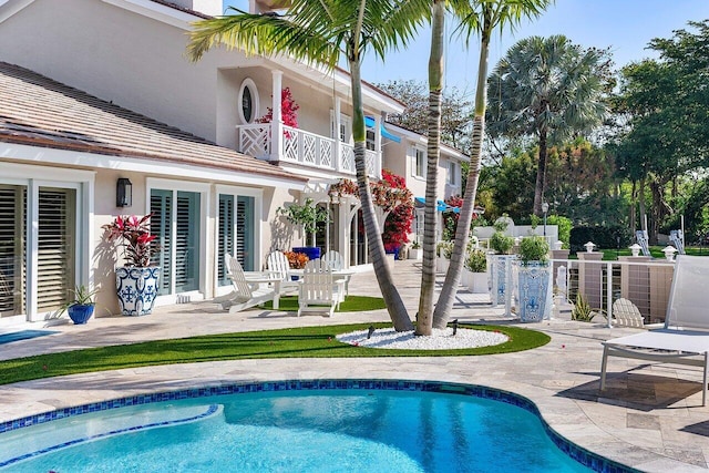 back of property featuring stucco siding, a patio area, an outdoor pool, fence, and a balcony