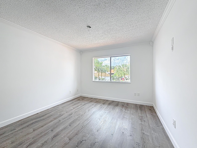 spare room featuring a textured ceiling, ornamental molding, light wood-style flooring, and baseboards