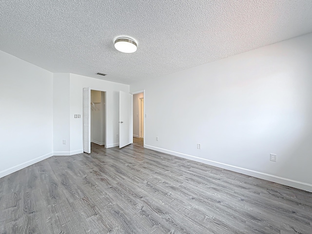 unfurnished room featuring a textured ceiling, light wood finished floors, visible vents, and baseboards