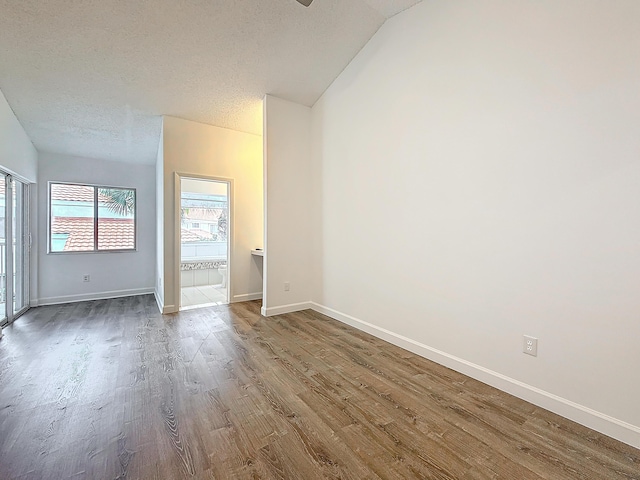 unfurnished room with vaulted ceiling, a textured ceiling, baseboards, and wood finished floors