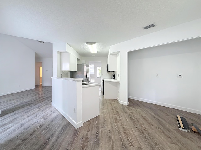 kitchen featuring stainless steel fridge, visible vents, white cabinets, open floor plan, and a peninsula