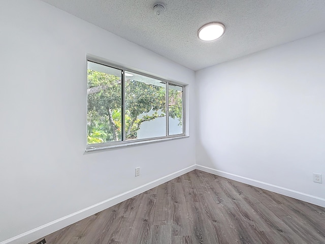 unfurnished room with a textured ceiling, wood finished floors, and baseboards