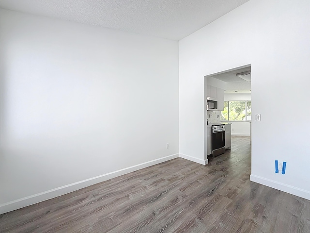 spare room with a textured ceiling, baseboards, and wood finished floors