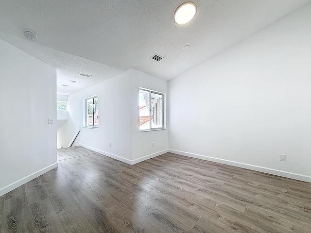 empty room with baseboards, a textured ceiling, visible vents, and wood finished floors