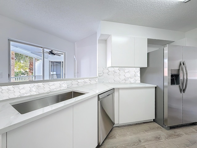 kitchen with appliances with stainless steel finishes, white cabinets, a sink, and light stone countertops