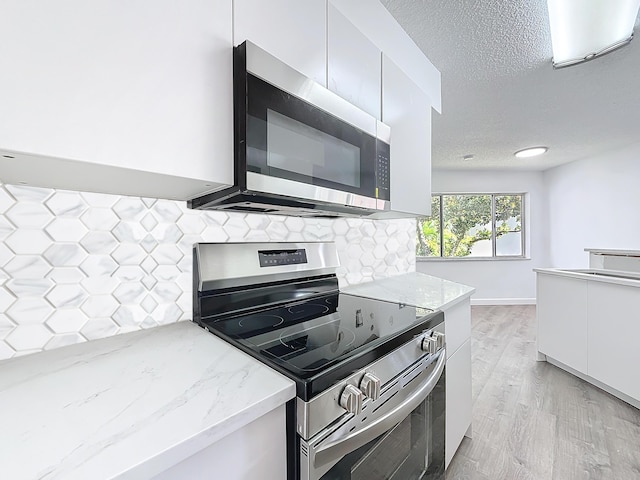 kitchen with light stone counters, backsplash, appliances with stainless steel finishes, white cabinets, and modern cabinets