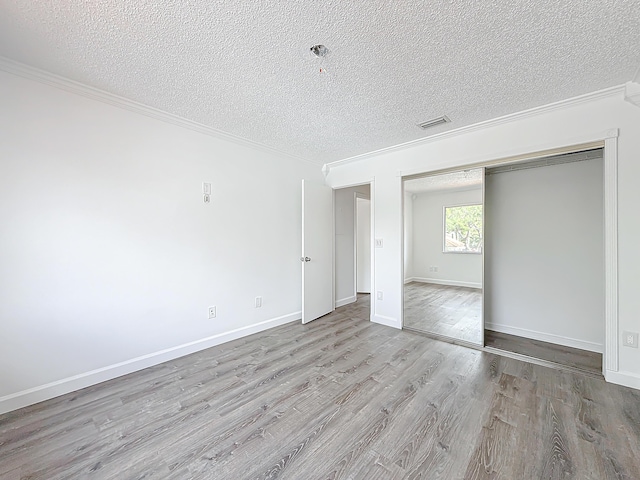 unfurnished room with crown molding, visible vents, a textured ceiling, light wood-type flooring, and baseboards