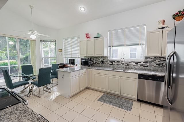 kitchen featuring light tile patterned floors, stainless steel appliances, a peninsula, a sink, and decorative backsplash