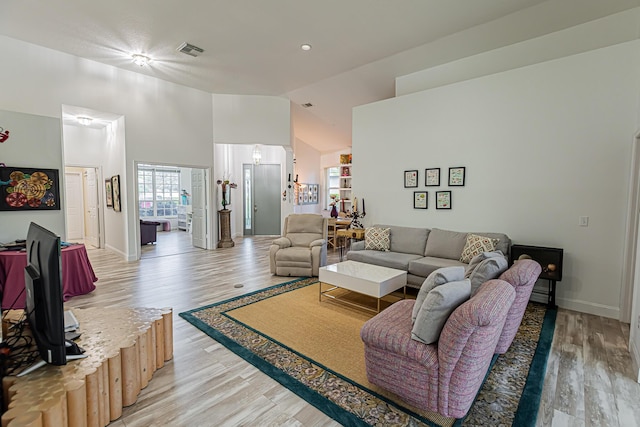 living room featuring light wood-style floors, baseboards, visible vents, and high vaulted ceiling