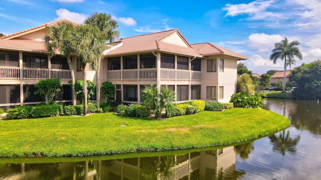 exterior space featuring a water view, a sunroom, a lawn, and a tiled roof