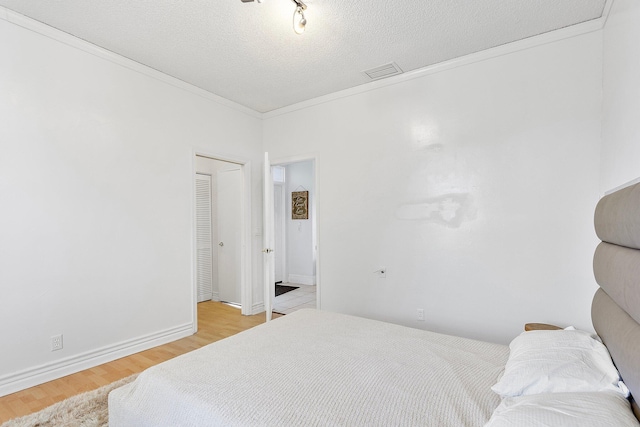 bedroom featuring a textured ceiling, visible vents, baseboards, light wood finished floors, and crown molding