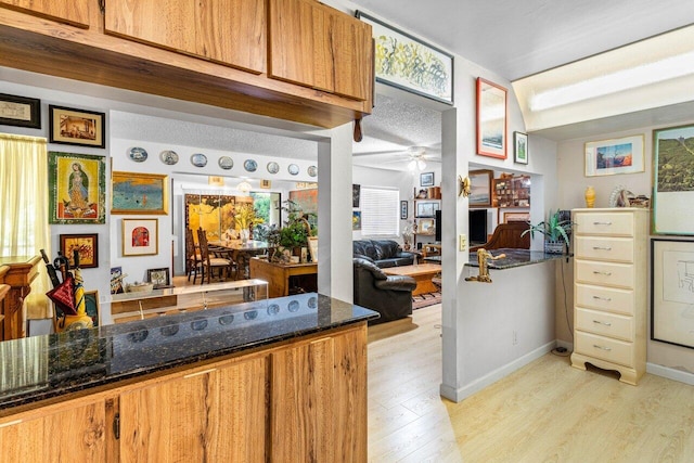 kitchen featuring kitchen peninsula, light hardwood / wood-style flooring, a textured ceiling, ceiling fan, and dark stone counters