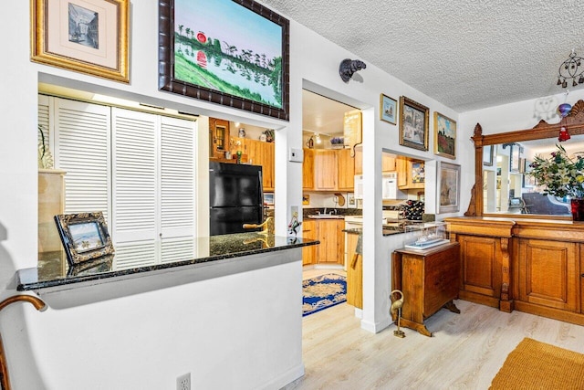 kitchen with light hardwood / wood-style flooring, black refrigerator, a textured ceiling, dark stone counters, and sink