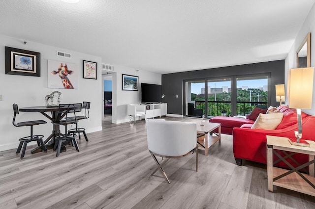 living room with a textured ceiling, wood finished floors, visible vents, and baseboards