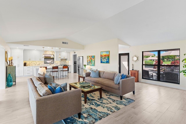 living area with light wood-style floors, visible vents, and high vaulted ceiling