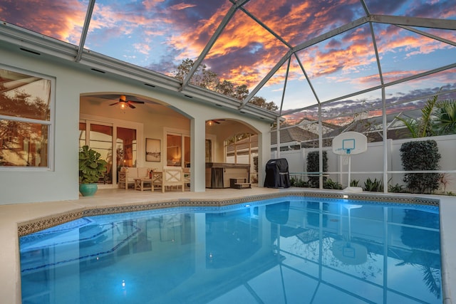 pool at dusk featuring glass enclosure, a patio, fence, a fenced in pool, and ceiling fan