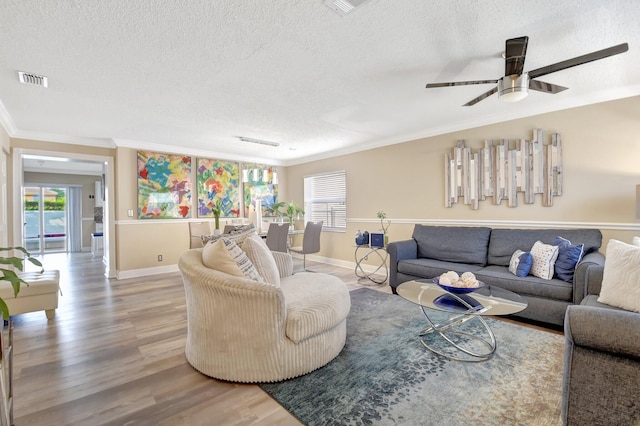 living room with visible vents, ornamental molding, a textured ceiling, wood finished floors, and baseboards
