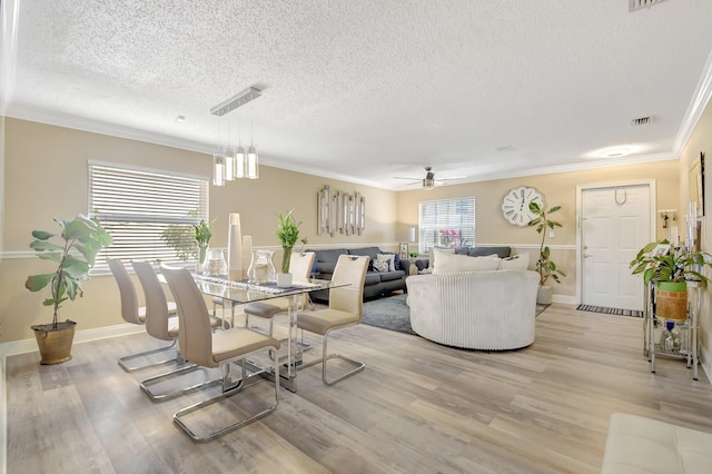dining space with baseboards, visible vents, ornamental molding, a textured ceiling, and light wood-style floors