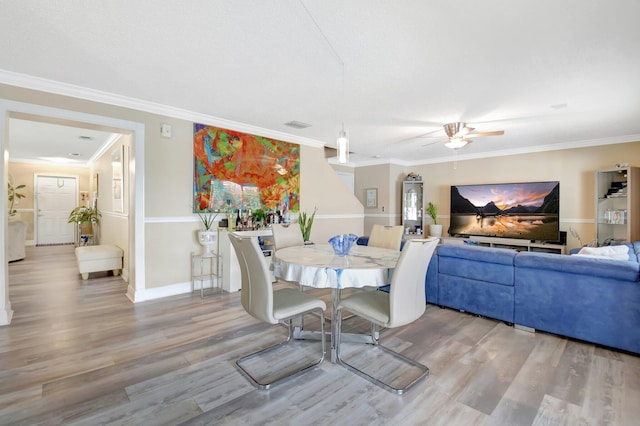 dining room with baseboards, visible vents, a ceiling fan, ornamental molding, and light wood-type flooring