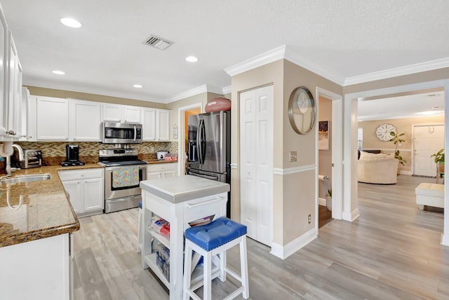 kitchen featuring stainless steel appliances, a kitchen island, a sink, visible vents, and white cabinetry