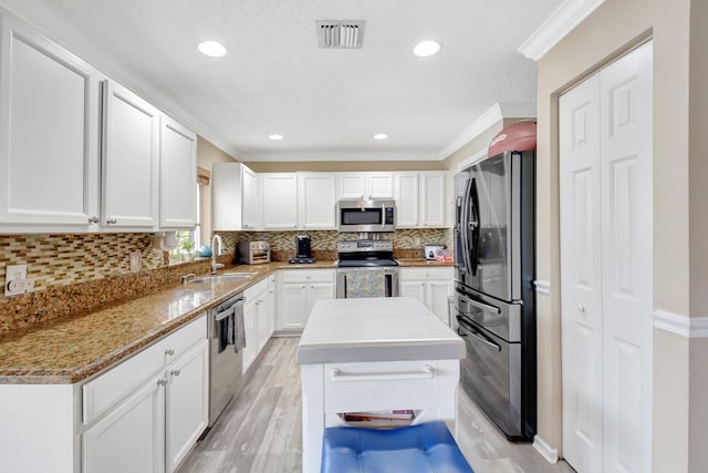 kitchen with visible vents, stainless steel appliances, crown molding, white cabinetry, and a sink